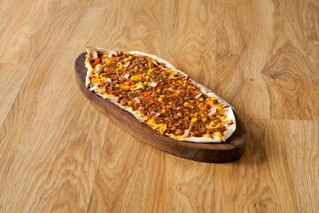 Turkish pide with minced meat and vegetables on a wooden platter.
