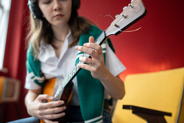 Girl musician plays balalaika in headphones, syncing to melody for training chords and notes. Woman...
