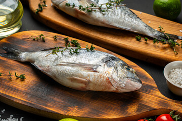 Two Fresh, raw dorado fish on a wooden board on a black background with leeks, lime, olive oil and cherry tomatoes on the table ready for cooking. Space for text