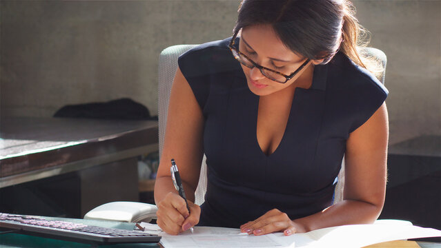 Close Up Of Businesswoman Wearing Glasses Sitting At Desk In Office Making Notes On Document Files