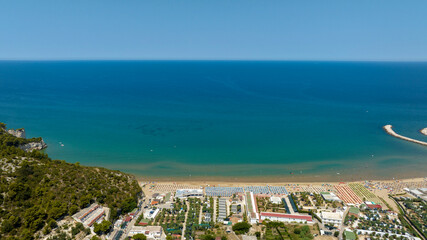 Fototapeta premium Aerial view of the beach of Peschici bay, in Puglia, Italy, on the coast of the Adriatic Sea. It's a tourist destination in Gargano, in the province of Foggia. There are many beach clubs and umbrellas