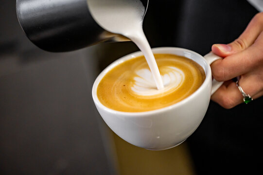 close-up of a barista pouring steamed milk into a cup of coffee, creating a beautiful latte art design. The warm tones of the drink contrast with the sleek background. Perfect for coffee enthusiasts.