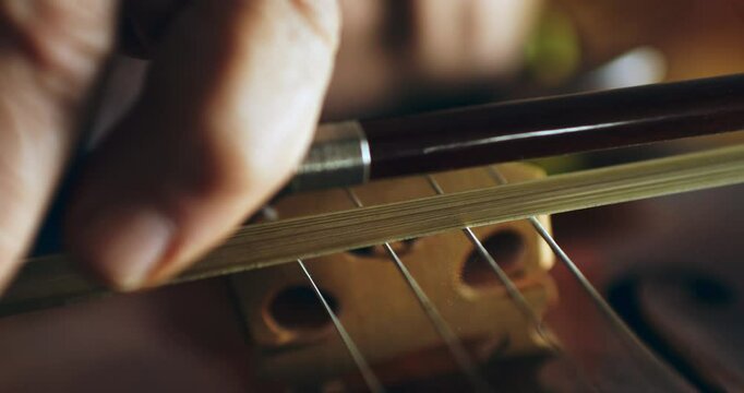 Super slow motion macro of master luthiers hands draw bow across strings of handmade violin at 1000 fps. Each movement showcase precision and artistry in both playing and craftsmanship of instrument