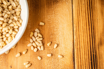 Pine nuts in a white bowl on a wooden background. Top view