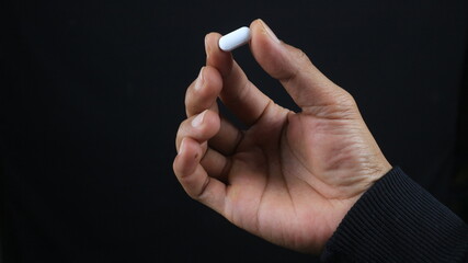 Close up male hand holding drug capsule, black background Pharmacy and medicine concept