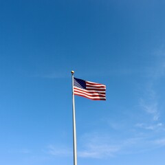 The American flag waving in the wind with a blue sky.