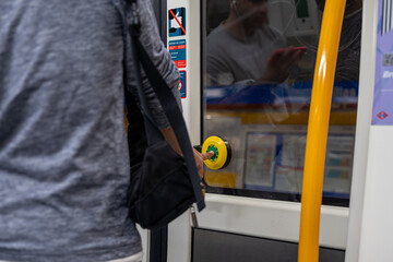 A man is standing in front of a bus door, holding a yellow button. The man is wearing a grey shirt...