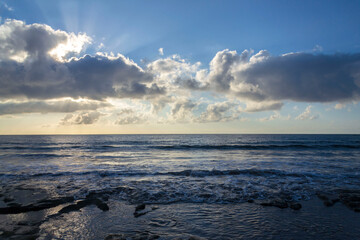 Obraz premium Breathtaking sunrise with sun hiding behind cloud, sea waves and blue sky with copy space