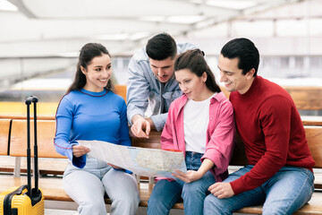 Two young couples are gathered at an airport, examining a map and discussing their travel plans. They appear excited about their upcoming adventure, enjoying each other's company.