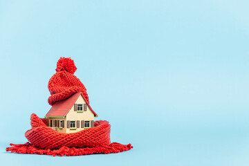 thermal insulation of buildings: tiny model house with red scarf and bobble hat, blue background
