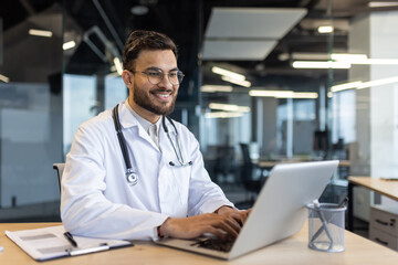 Smiling doctor working on a laptop in a professional office. The setting emphasizes modern...