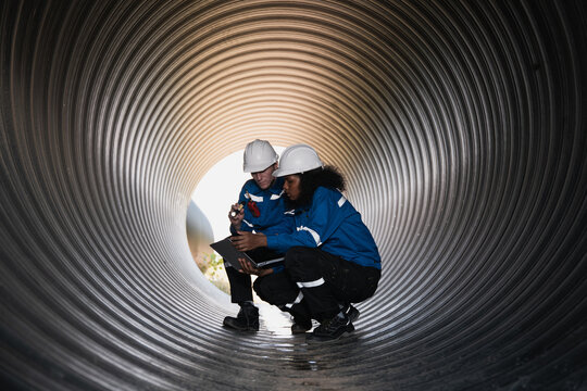 Workers inside a big steel pipe building a pipeline for oil, gas, and fuel at an industrial site.
