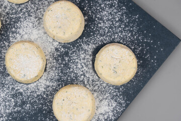 Frozen syrniki (cottage cheese pancakes) flavored with creamy cheese and dill on a dark black background, semi-finished and ready for cooking. 