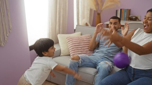Family spending quality time together playing with a purple balloon in a cozy living room setting, with a man, woman, and child expressing joy and connection