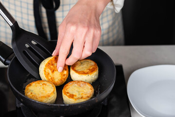 Hands of a female chef frying and baking homemade savory syrniki (cottage cheese pancakes) with creamy cheese and dill in a pan, sizzling in oil. Concept of home cooking and traditional recipes