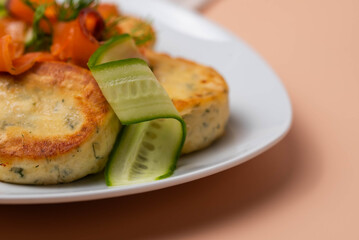 Syrniki with creamy cheese and dill, served on plate with fresh cucumber slices, thinly sliced smoked salmon, and herbs. Concept of traditional home recipes, and balanced meals.