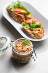 Homemade chicken liver pate in a glass jar, served with whole-grain bread topped with pate, fresh tomato slices, and arugula. A rustic and flavorful dish perfect for breakfast or a light snack.