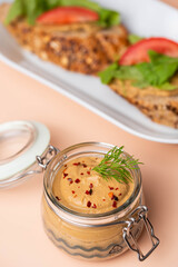 Homemade chicken liver pate in a glass jar, served with whole-grain bread topped with pate, fresh tomato slices, and arugula. A rustic and flavorful dish perfect for breakfast or a light snack.