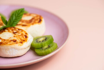 Sweet classic breakfast syrniki (cottage cheese pancakes) served on a plate, with vibrant slices of grapefruit, fresh kiwi, and mint. Home cooking, traditional recipes, and delicious morning meals.