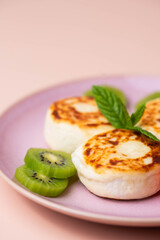Sweet classic breakfast syrniki (cottage cheese pancakes) served on a plate, with vibrant slices of grapefruit, fresh kiwi, and mint. Home cooking, traditional recipes, and delicious morning meals.