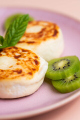 Sweet classic breakfast syrniki (cottage cheese pancakes) served on a plate, with vibrant slices of grapefruit, fresh kiwi, and mint. Home cooking, traditional recipes, and delicious morning meals.