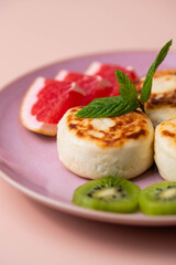 Sweet classic breakfast syrniki (cottage cheese pancakes) served on a plate, with vibrant slices of grapefruit, fresh kiwi, and mint. Home cooking, traditional recipes, and delicious morning meals.