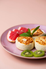 Sweet classic breakfast syrniki (cottage cheese pancakes) served on a plate, with vibrant slices of grapefruit, fresh kiwi, and mint. Home cooking, traditional recipes, and delicious morning meals.
