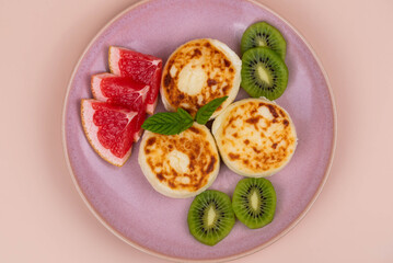 Sweet classic breakfast syrniki (cottage cheese pancakes) served on a plate, with vibrant slices of grapefruit, fresh kiwi, and mint. Home cooking, traditional recipes, and delicious morning meals.