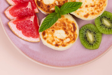 Sweet classic breakfast syrniki (cottage cheese pancakes) served on a plate, with vibrant slices of grapefruit, fresh kiwi, and mint. Home cooking, traditional recipes, and delicious morning meals.