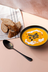 Creamy pumpkin soup served in deep bowl, topped with a swirl of cream and garnished with fresh herbs. A comforting, hearty dish perfect for autumn evenings, blending smooth textures and rich flavors.
