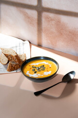 Creamy pumpkin soup served in deep bowl, topped with a swirl of cream and garnished with fresh herbs. A comforting, hearty dish perfect for autumn evenings, blending smooth textures and rich flavors.