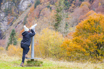 Mujer mirando a través de un telescopio en un bosque otoñal