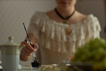 Close up of young woman dipping pen in ink while preparing to write on parchment in classic...