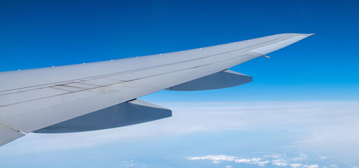 Fototapeta premium Wing of airplane flying above the clouds in the blue sky background.