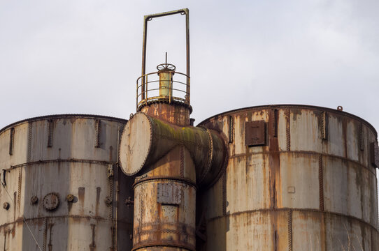 Rusty industrial tanks and pipes reaching for the cloudy sky