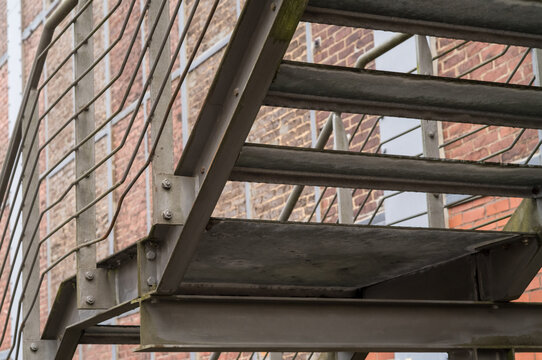 Metal fire escape stairs with caged mesh wire alongside brick building - Powered by Adobe