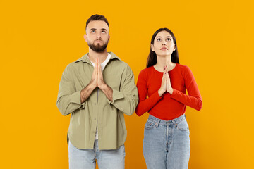 A young Caucasian couple stands side by side, their hands clasped together in a gesture of love and devotion. The vibrant yellow background enhances their connection and warmth.