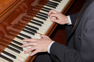 Close up of unrecognizable man playing piano with male hands on black and white keyboard during classical concert, shot with camera flash