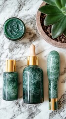 Three elegant green skincare bottles alongside a jar and a stone massager display on a marble countertop with a succulent plant in a pot