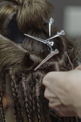 Naklejka premium Process of braiding dreadlocks, close-up. Human hair, hairdressing clips and hairdressers fingers at work, vertical image, selective focus.