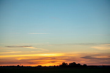Obraz premium Autumn landscape in the meadow on the background of forest and sunset sky with clouds illuminated by the setting sun