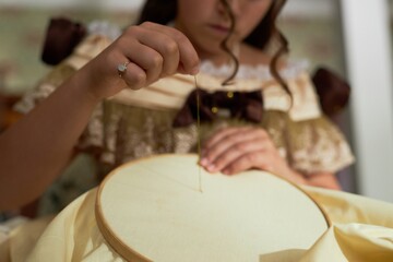 Close up of young lady guiding thread through fabric doing intricate embroidery in vintage setting,...