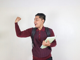 Young winner smart asian boy student he wear maroon t-shirt casual clothes backpack bag hold books showing hand biceps muscles isolated on white background. High school university college concept