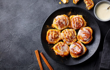 Cinnamon rolls, buns, cinnabons on black plate. Dark background. Close up. Copy space.