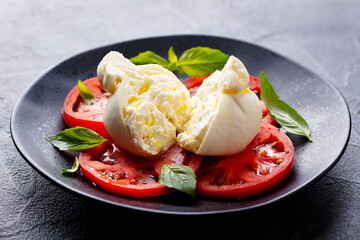 Caprese salad with tomatoes, burrata cheese and basil. Grey background. Close up.