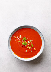 Tomato soup with fresh herbs and pine nuts in a bowl. Grey stone background. Copy space. Top view.