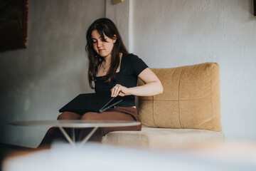 A young female student sits in a comfy chair, opening her laptop, preparing to study at a stylish...
