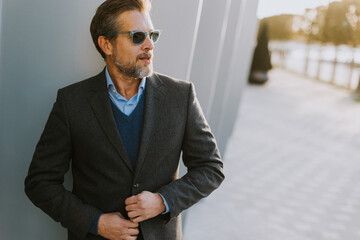 Stylish man adjusting his blazer while standing outdoors in the warm afternoon light