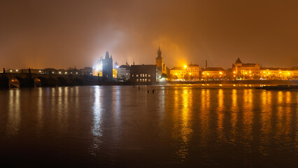 Monumental city of Prague at night with the illuminated buildings reflecting on the Vltava River.