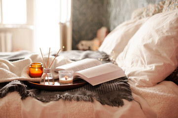 Home liquid perfume in glass bottle and sticks with open paper book and candles in bed close up. Relaxation. Cozy atmosphere.